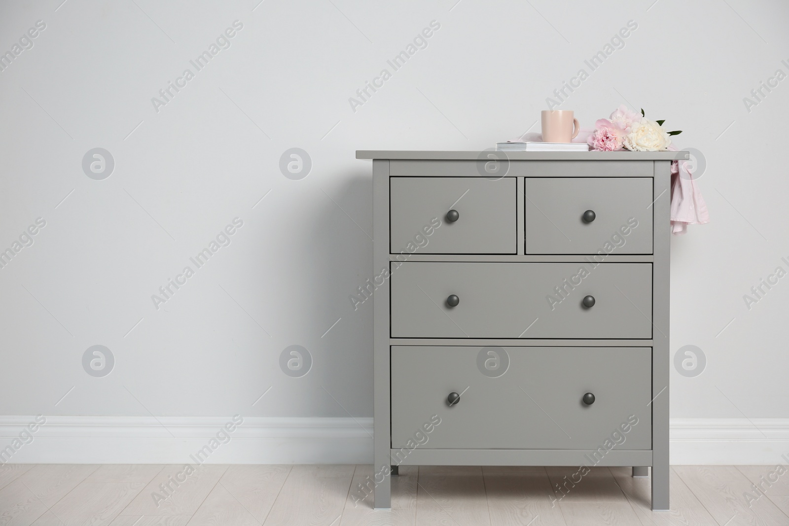 Photo of Grey chest of drawers near light wall. Space for text