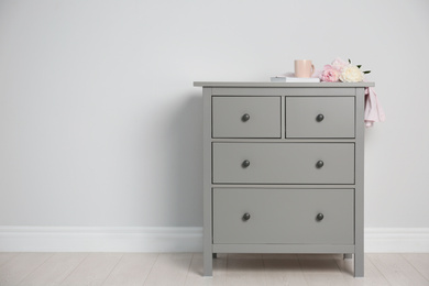 Photo of Grey chest of drawers near light wall. Space for text