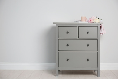 Grey chest of drawers near light wall. Space for text