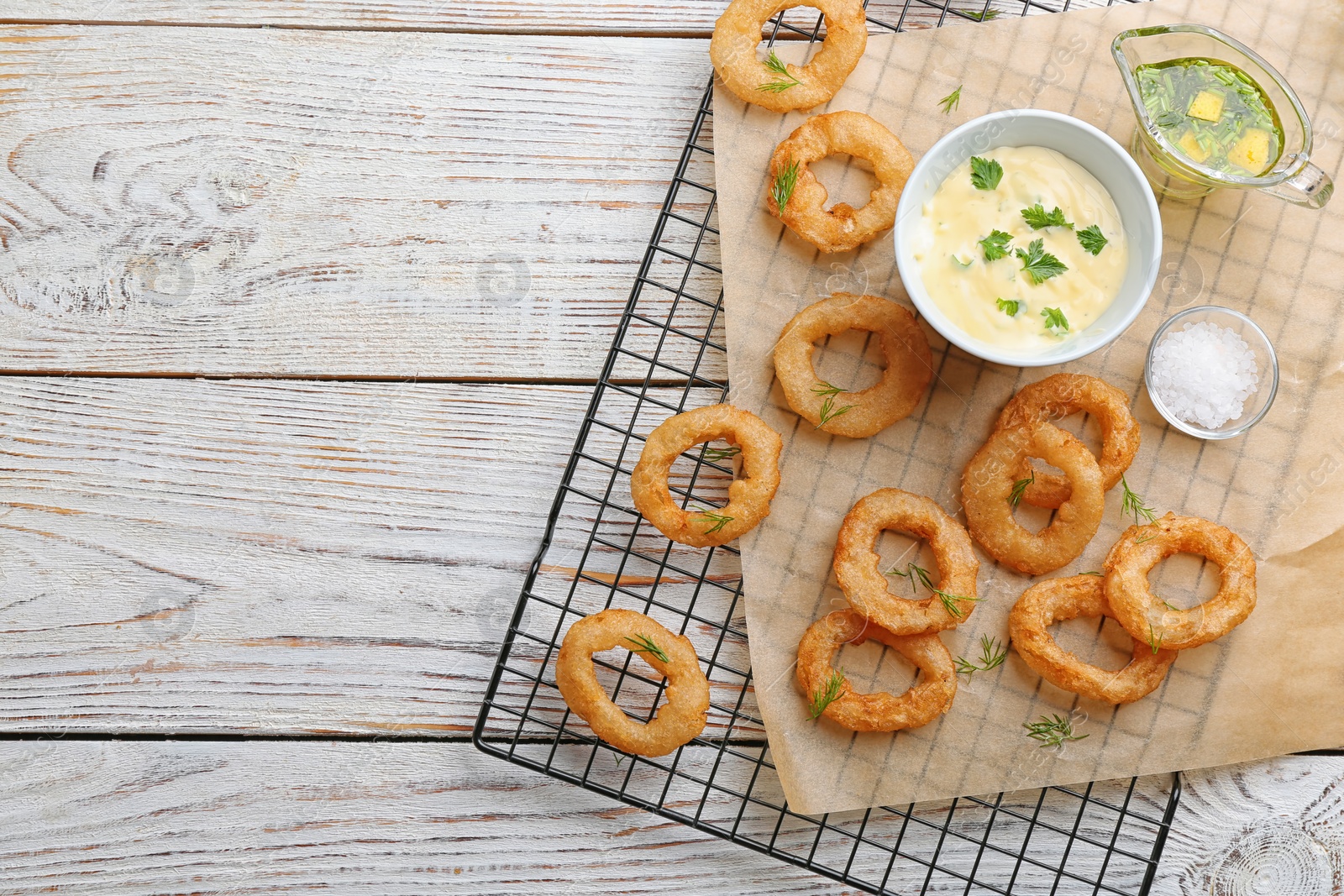 Photo of Cooling rack with fried onion rings and sauces on wooden background, top view