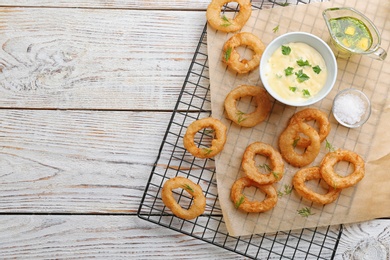 Photo of Cooling rack with fried onion rings and sauces on wooden background, top view