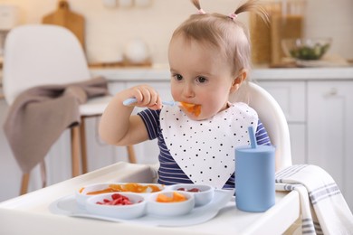 Photo of Cute little baby eating food in high chair at kitchen