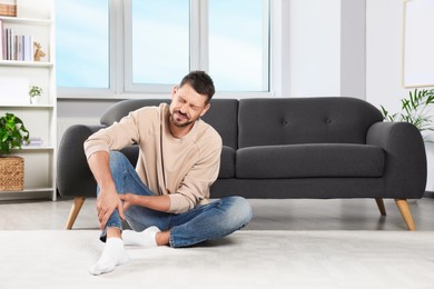 Photo of Man suffering from leg pain at home, space for text