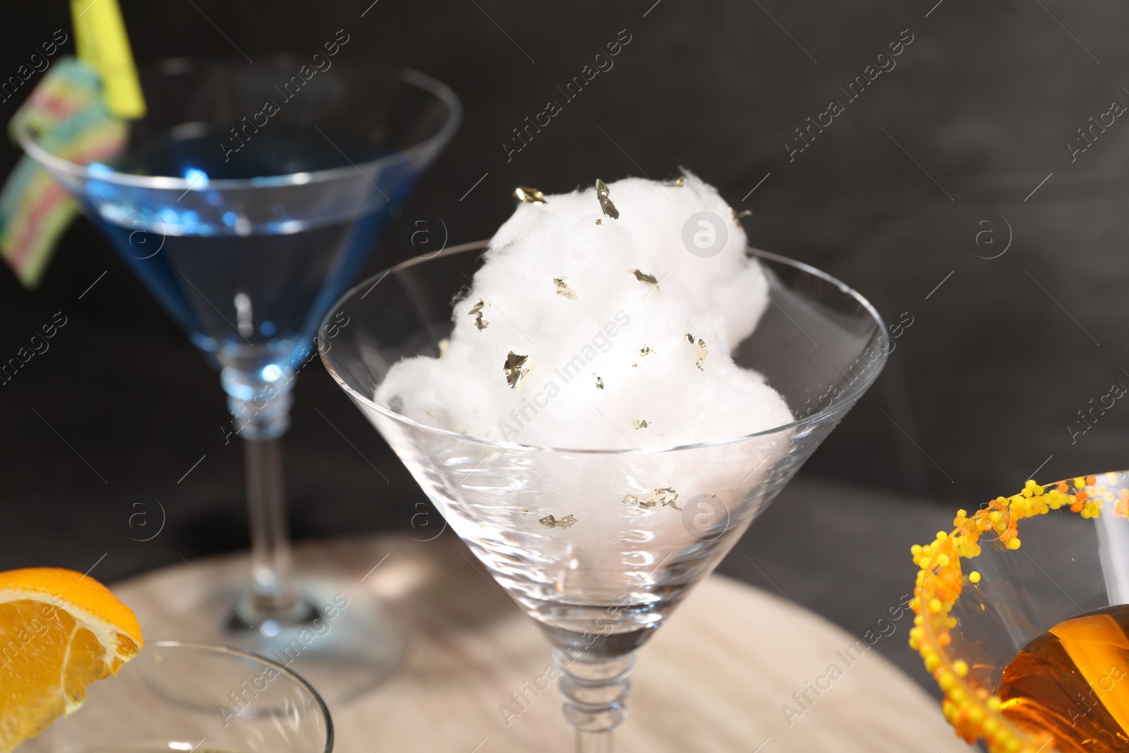 Photo of Tasty cotton candy cocktail and other alcoholic drinks in glasses on table against gray background, closeup