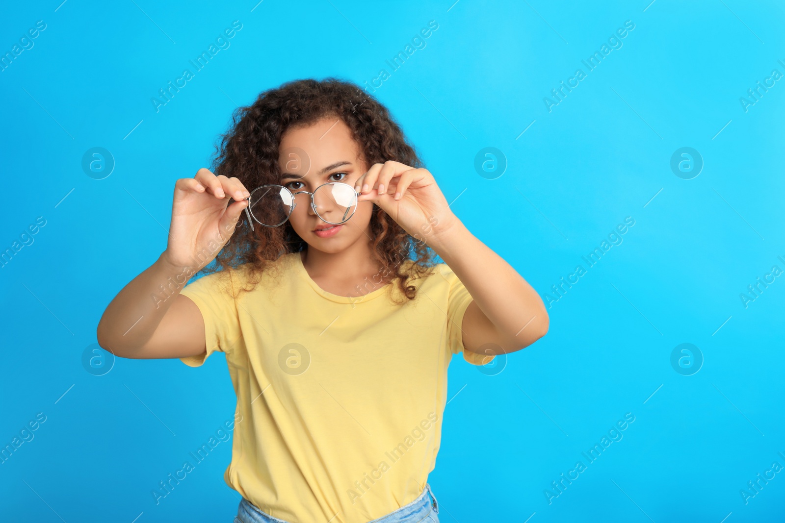 Photo of Young African-American woman with glasses on blue background. Vision problems