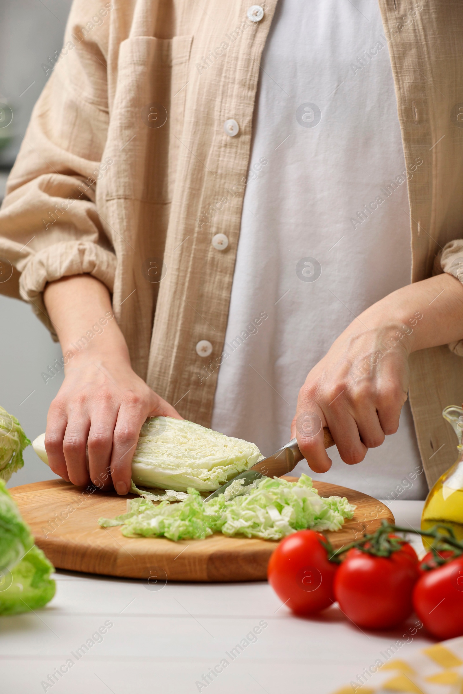 Photo of Woman cutting fresh chinese cabbage at white wooden table in kitchen, closeup