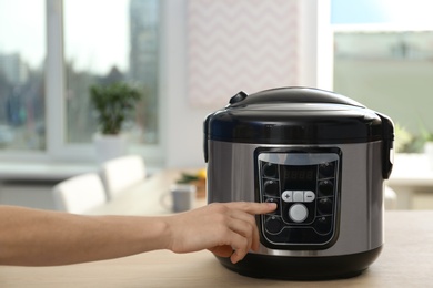 Woman turning on modern electric multi cooker in kitchen