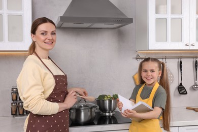 Cute little girl with her mother cooking by recipe book in kitchen