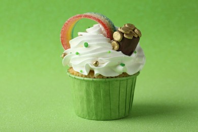 St. Patrick's day party. Tasty cupcake with sour rainbow belt and pot of gold toppers on green background, closeup