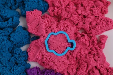 Bright kinetic sand and toy on white table, flat lay