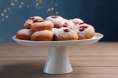 Photo of Stand with delicious Hanukkah donuts on wooden table against blurred festive lights
