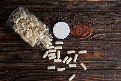 Photo of Medical bottle with pills on wooden table, flat lay