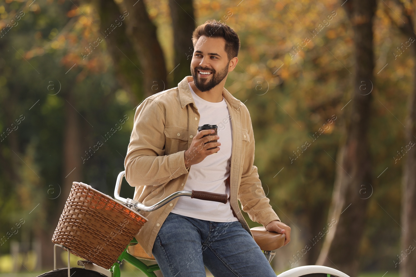 Photo of Young man with bicycle holding takeaway coffee in autumn park