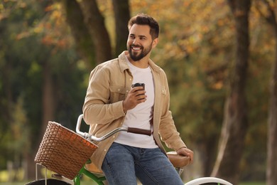 Young man with bicycle holding takeaway coffee in autumn park