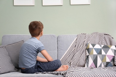 Photo of Lonely little boy sitting on sofa at home. Autism concept