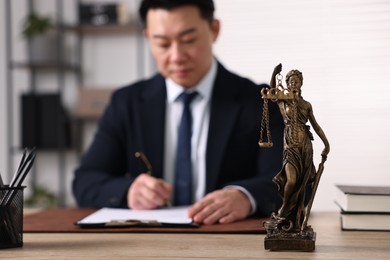 Photo of Notary working at wooden table in office, focus on statue of Lady Justice