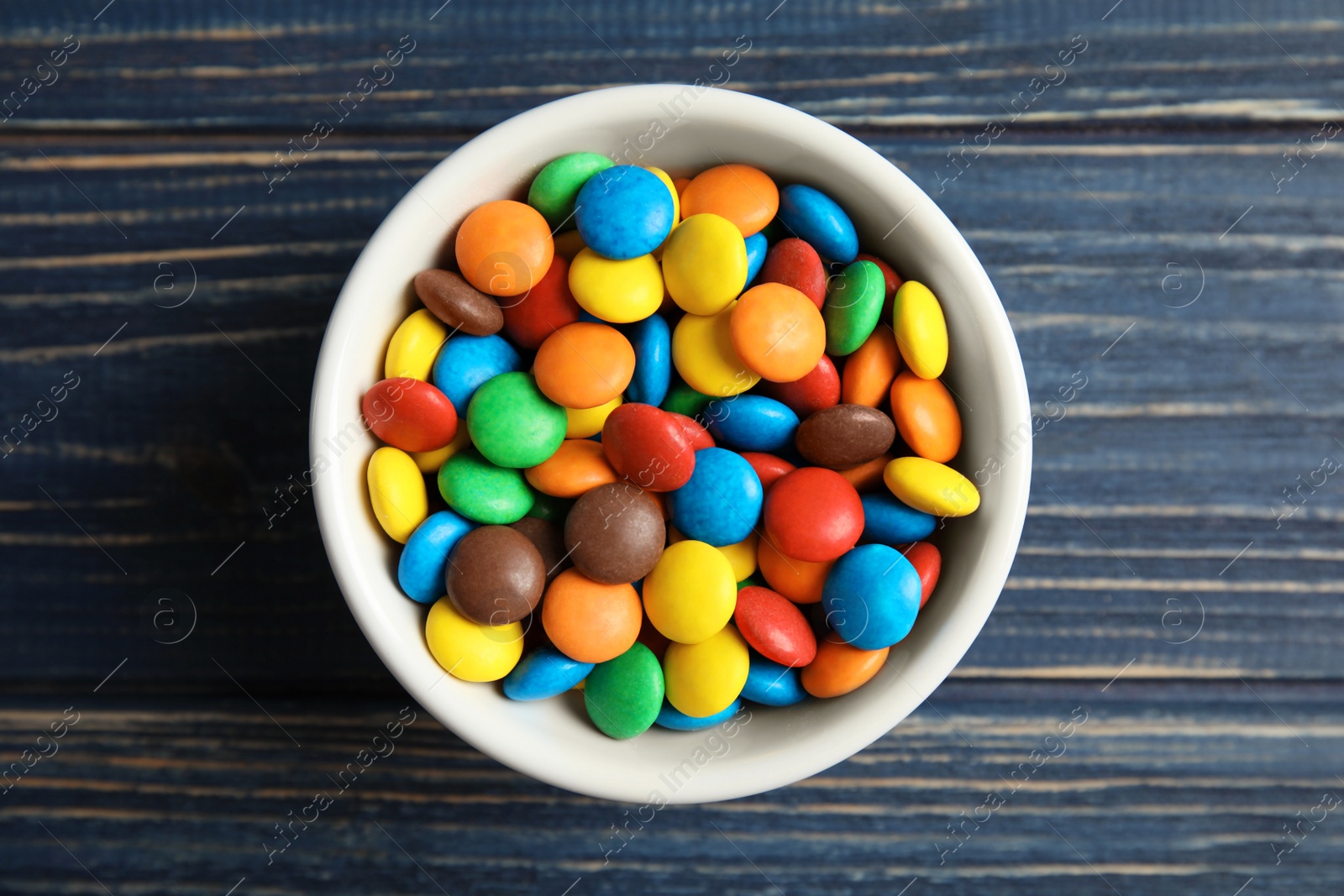 Photo of Bowl with colorful candies on wooden background, top view