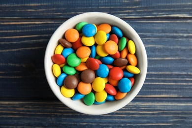 Photo of Bowl with colorful candies on wooden background, top view
