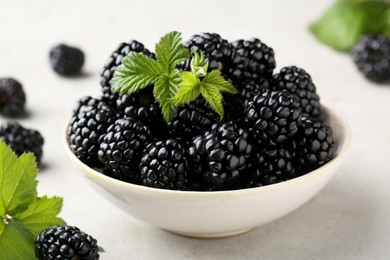 Photo of Bowl of fresh blackberries with leaves on white table
