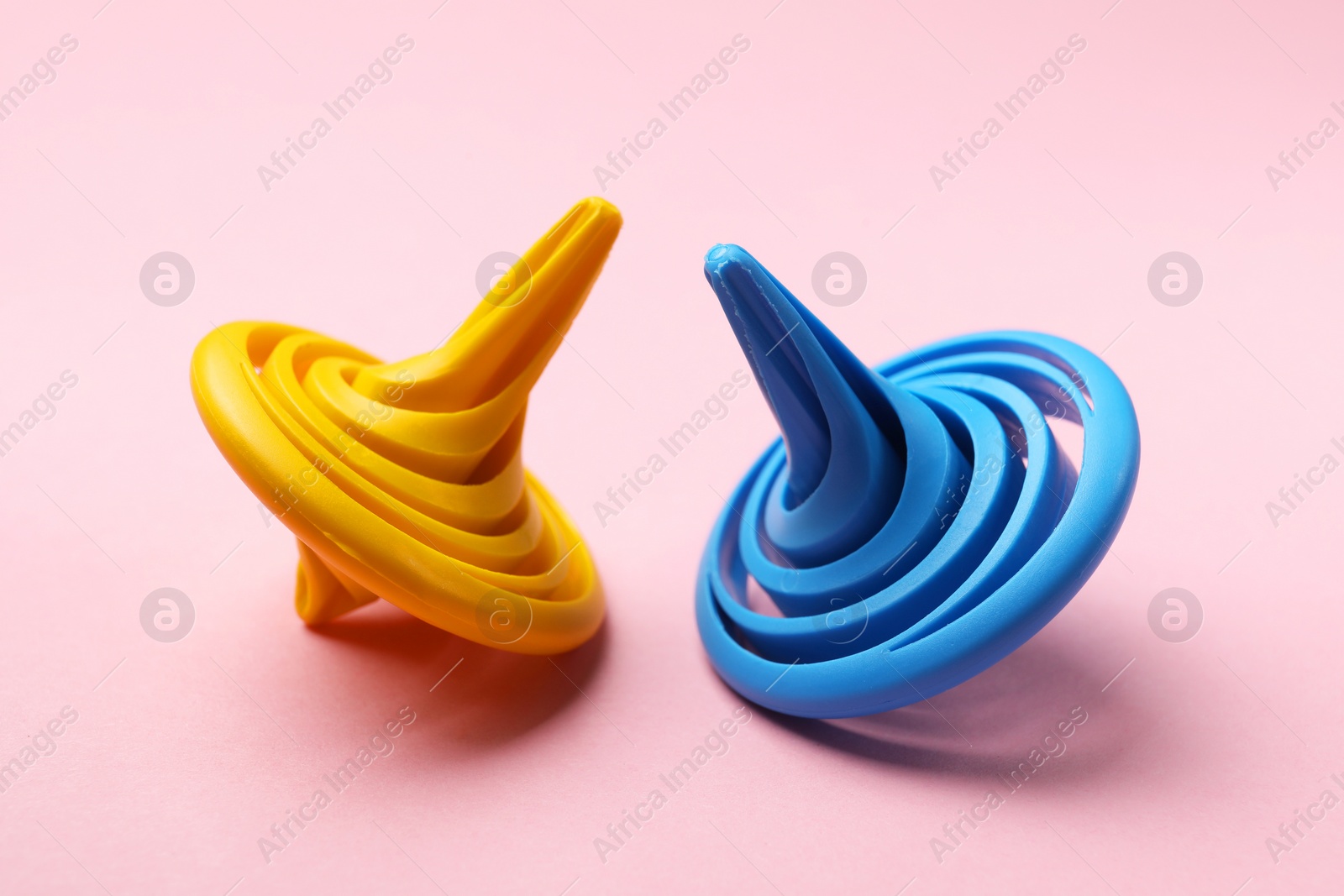 Photo of Yellow and blue spinning tops on pink background, closeup