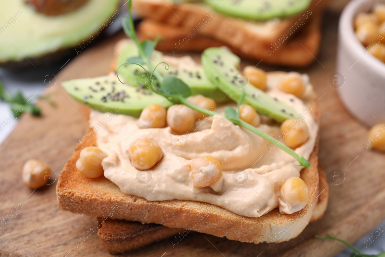 Photo of Delicious sandwich with hummus, avocado and chickpeas on wooden board, closeup