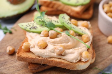 Delicious sandwich with hummus, avocado and chickpeas on wooden board, closeup