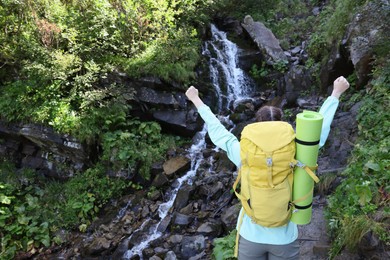 Tourist with backpack near stream in mountains, back view. Space for text