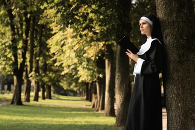 Photo of Young nun reading Bible in park on sunny day, space for text