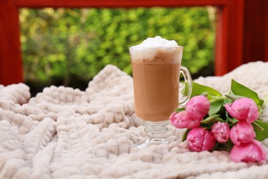 Photo of Glass of delicious cocoa and pink tulips on light blanket at terrace, space for text