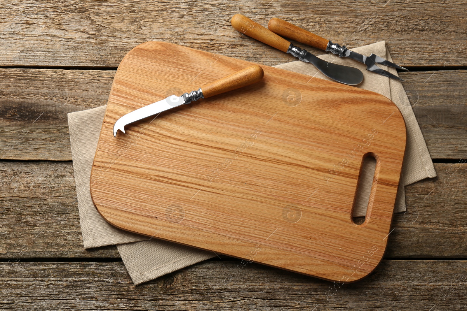 Photo of Cutting board, cheese knives and fork on old wooden table, flat lay
