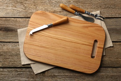 Photo of Cutting board, cheese knives and fork on old wooden table, flat lay