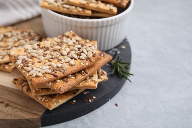 Photo of Cereal crackers with flax, sunflower and sesame seeds on grey table, closeup. Space for text