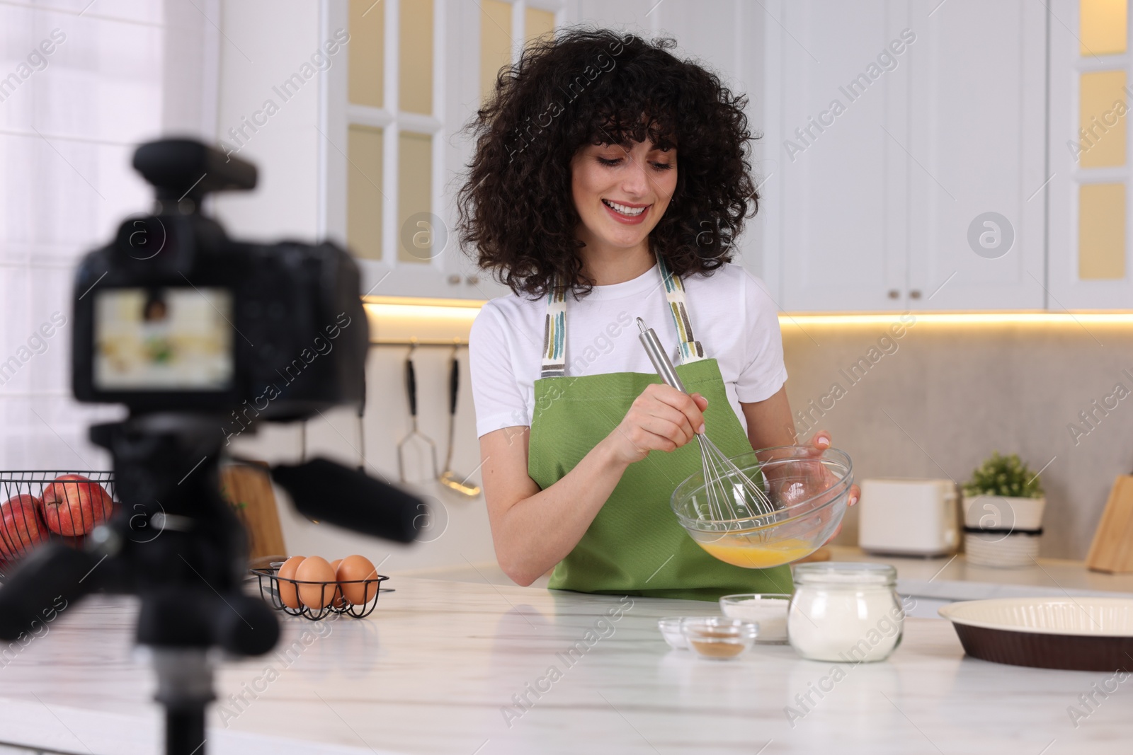 Photo of Smiling food blogger cooking while recording video in kitchen