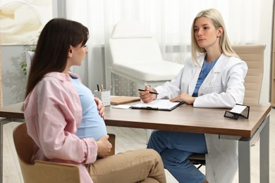 Doctor consulting pregnant patient at table in clinic