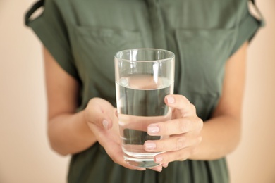 Photo of Woman holding glass with water on light background, closeup