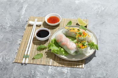 Photo of Tasty spring rolls served with sauces on grey textured table