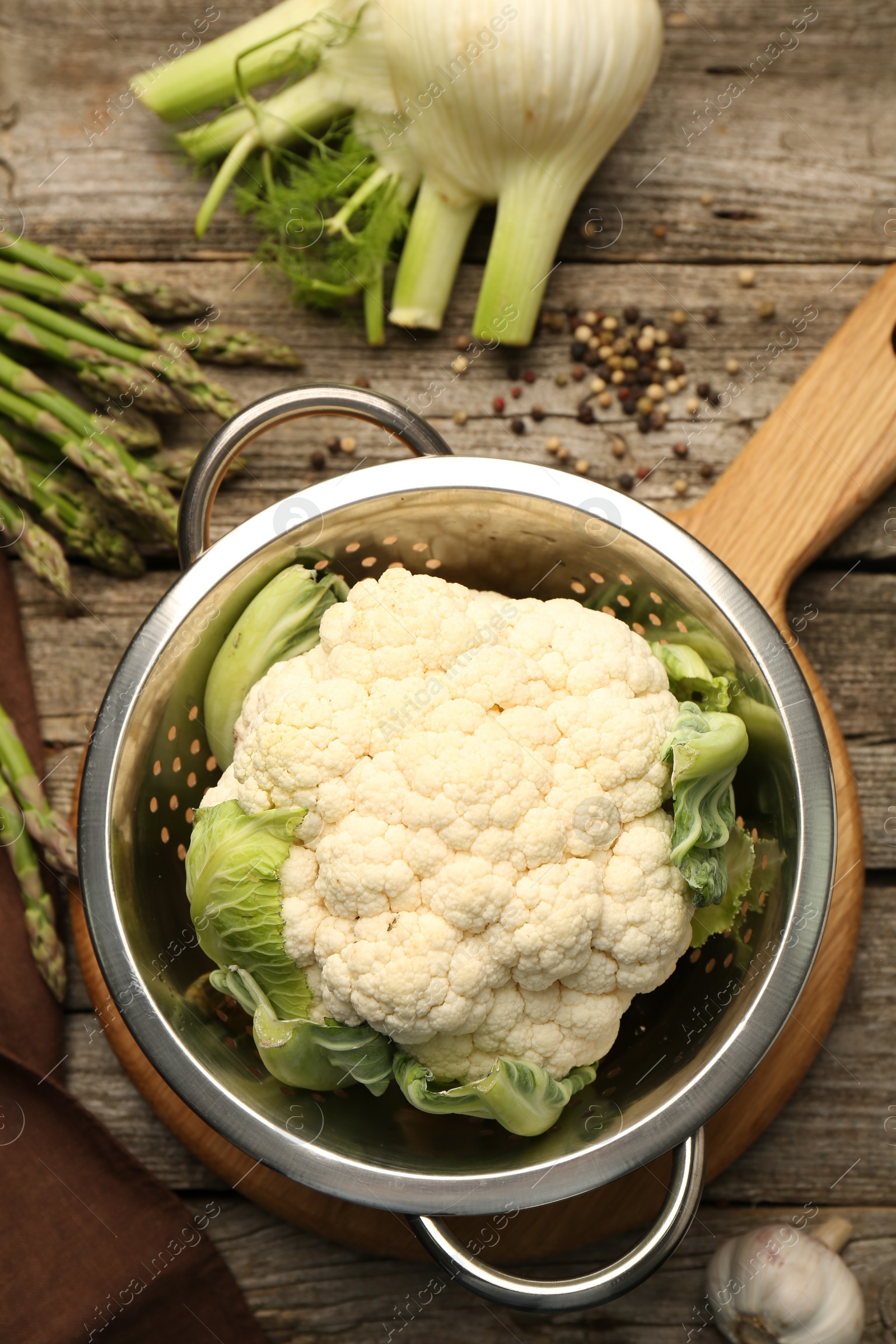 Photo of Metal colander with cauliflower, fennel and asparagus on wooden table, flat lay