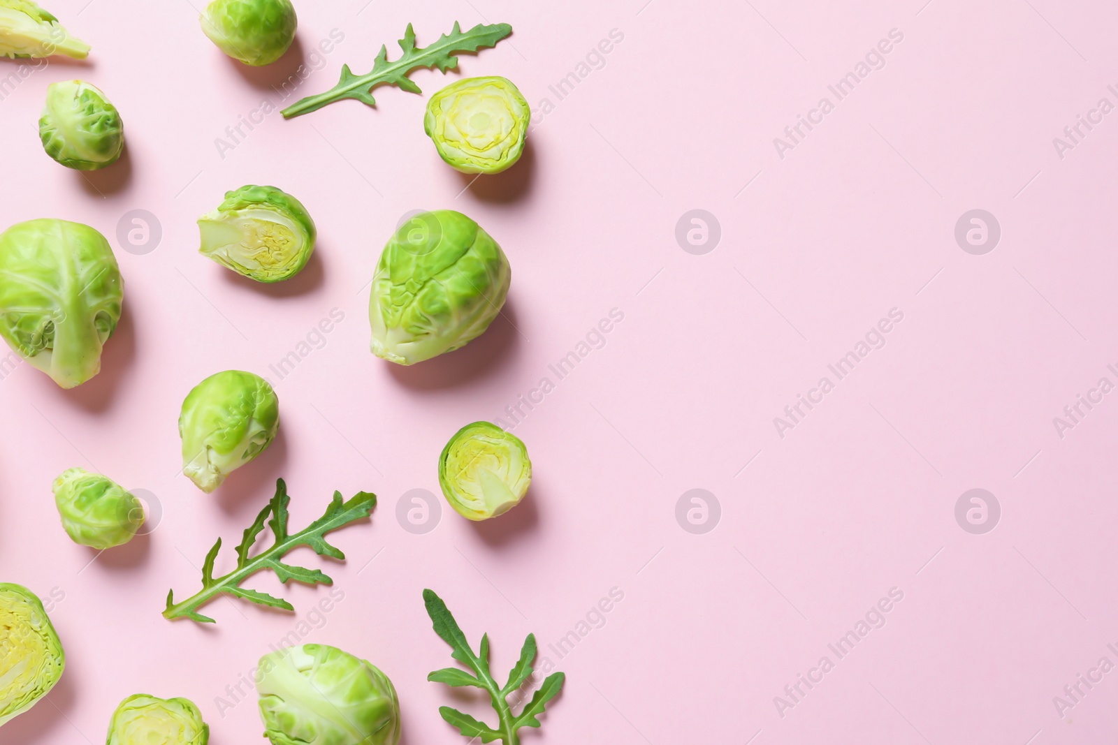 Photo of Fresh Brussels sprouts and arugula on color background, flat lay. Space for text