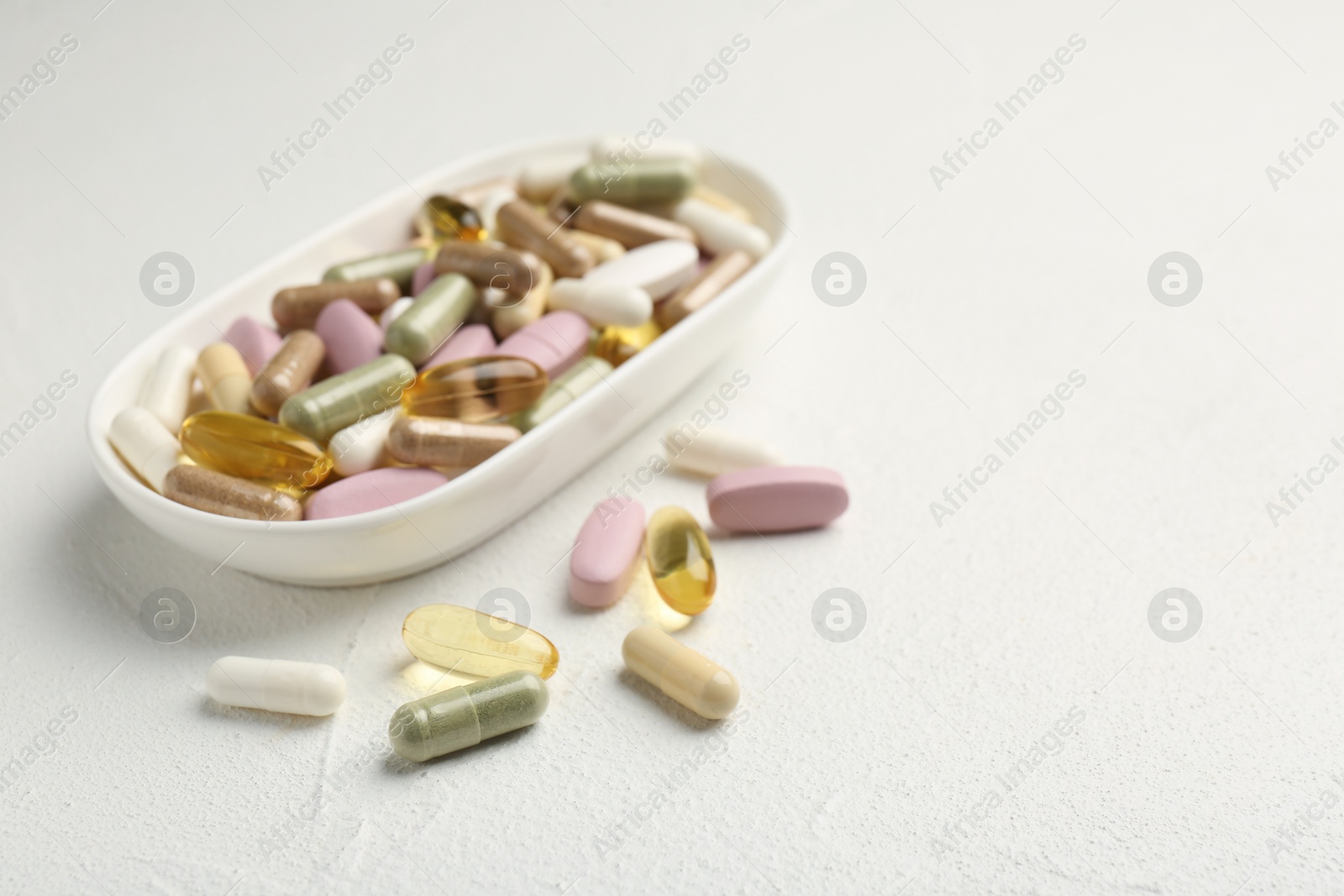 Photo of Different vitamin capsules in bowl on white wooden table, closeup. Space for text