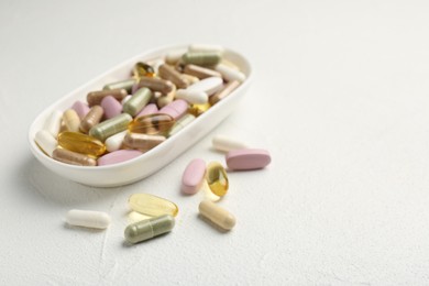 Different vitamin capsules in bowl on white wooden table, closeup. Space for text