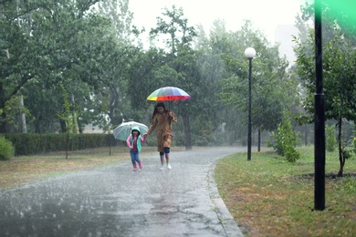 Mother and her daughter with umbrellas running outdoors on rainy day
