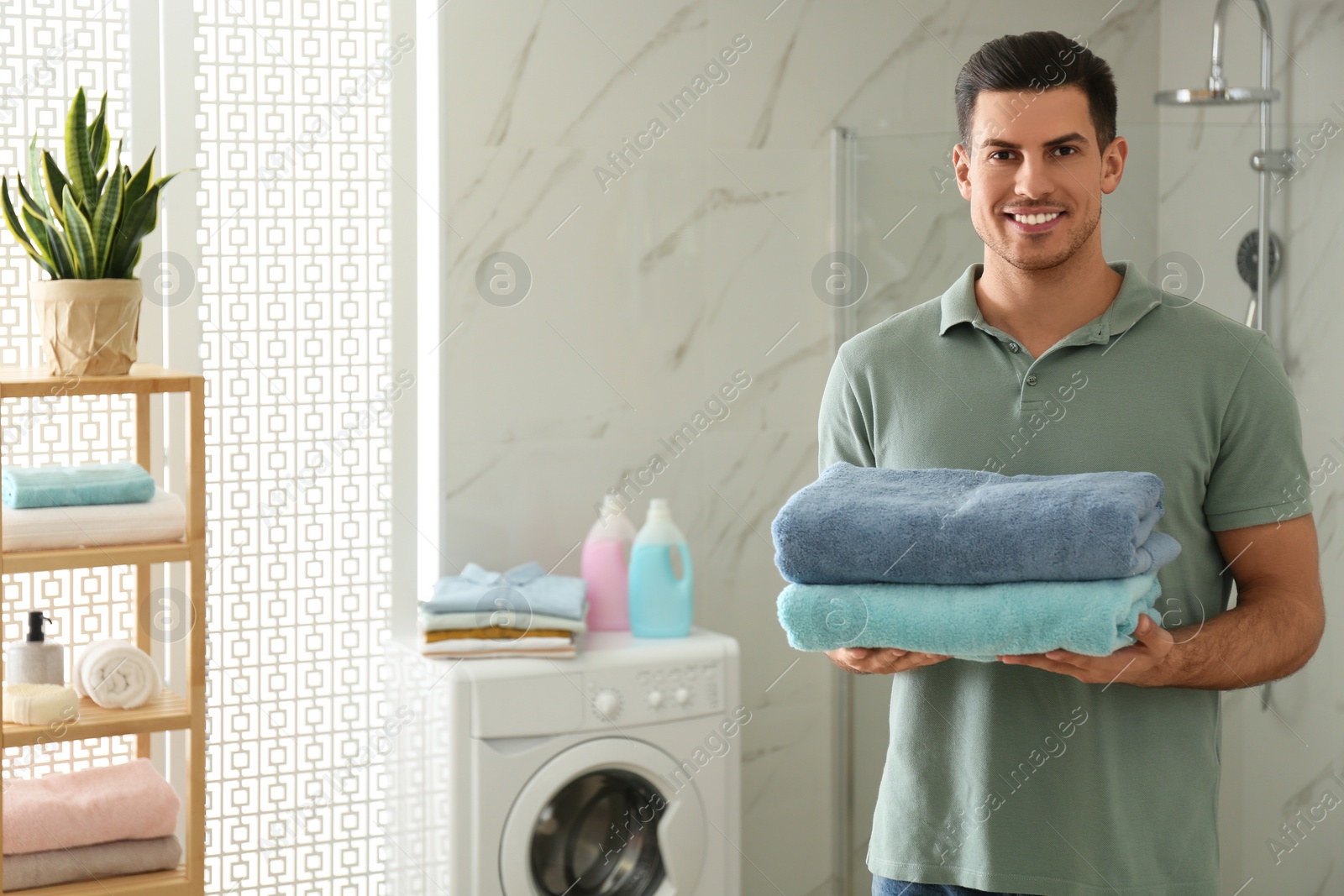 Photo of Happy man with clean towels in bathroom. Laundry day