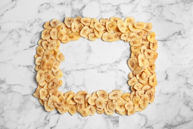 Photo of Frame made of sweet banana slices on marble background, top view with space for text. Dried fruit as healthy snack