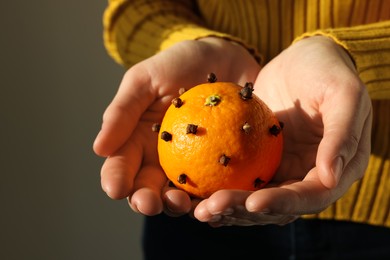 Photo of Woman holding pomander ball made of tangerine with cloves on grey background, closeup