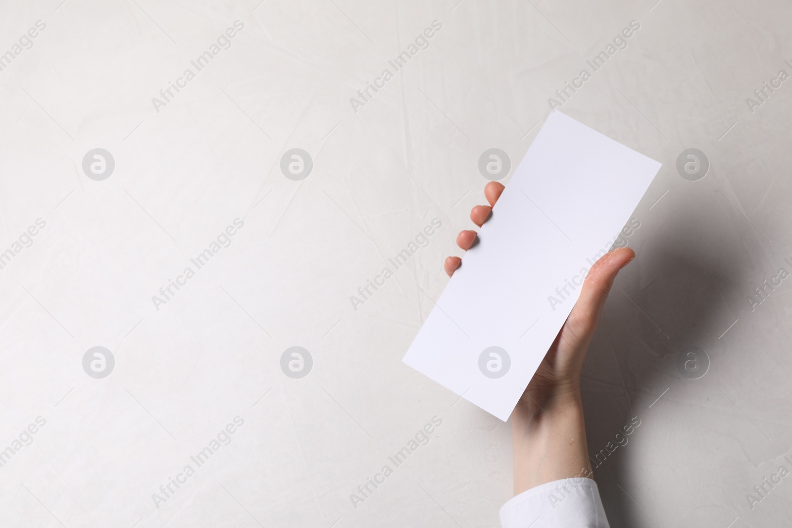 Photo of Woman holding blank card at white table, top view. Mockup for design