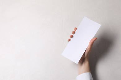 Woman holding blank card at white table, top view. Mockup for design