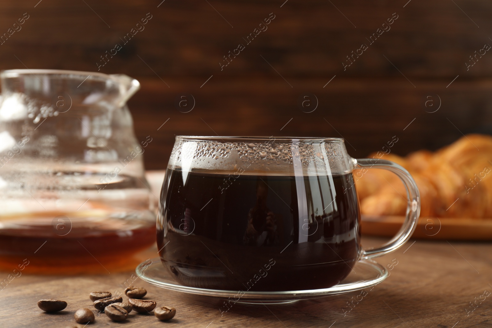 Photo of Hot coffee in glass cup and beans on wooden table, closeup