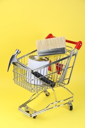 Photo of Small shopping cart with paint and renovation equipment on yellow background