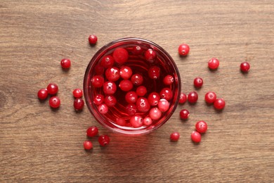 Photo of Tasty cranberry juice in glass and fresh berries on wooden table, top view