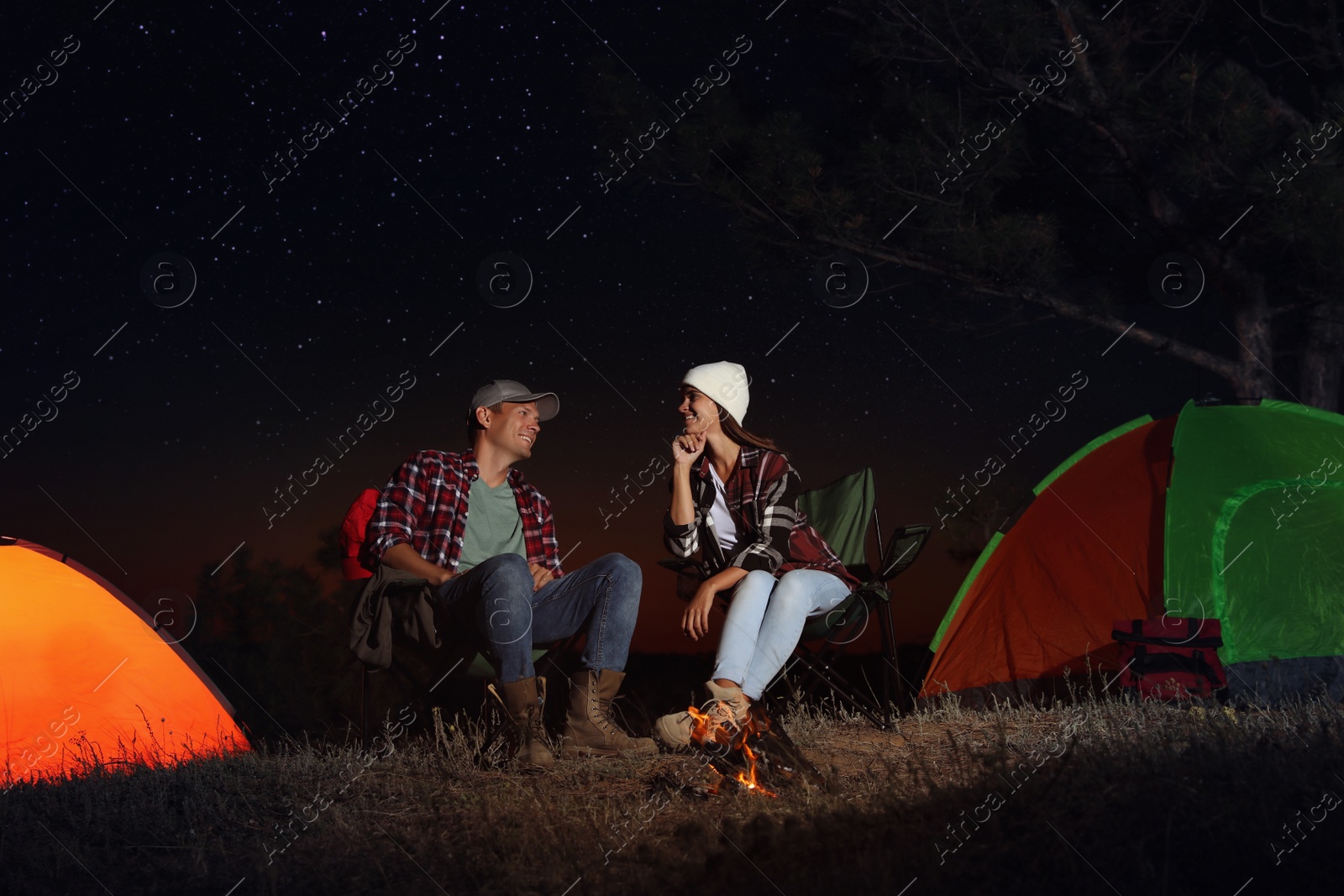 Photo of Couple near bonfire at night. Camping season